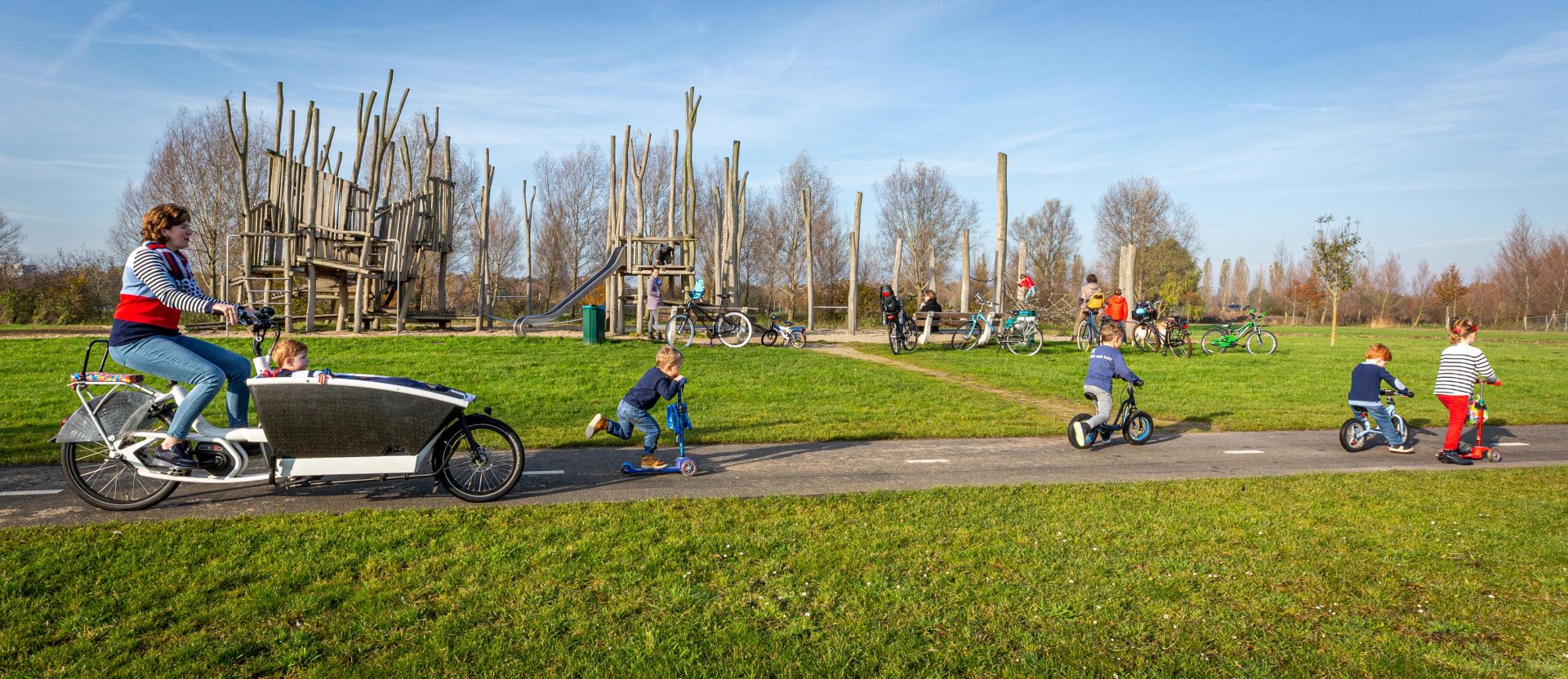 Een moeder met haar kinderen fietst langs de speeltuin in de Ruigenhoekse Polder