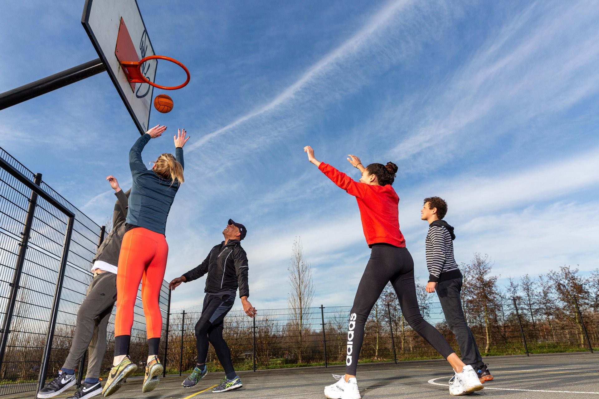 Vijf jongvolwassenen spelen een potje basketbal in Noorderpark Ruigenhoek