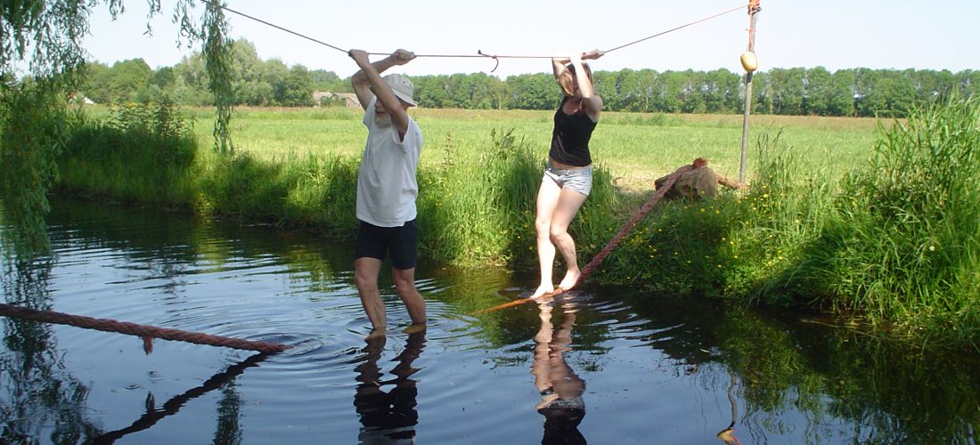 Een man en een vrouw steken het water over via een touwbrug