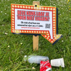 bord in het gras met lampjes erop waarop staat: deze kans laat je toch niet liggen? Elk stuk afval kan een winnend lot zijn t.w.v. €1.000,- speel gratis mee op trashorcash.nl en een QR-code. 